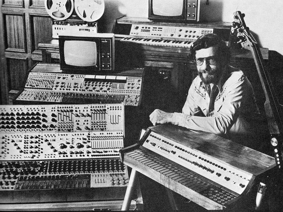 A Photograph of Don Buchla with an assortment of his creations from across his career. Photo courtesy of BuchlaUSA.