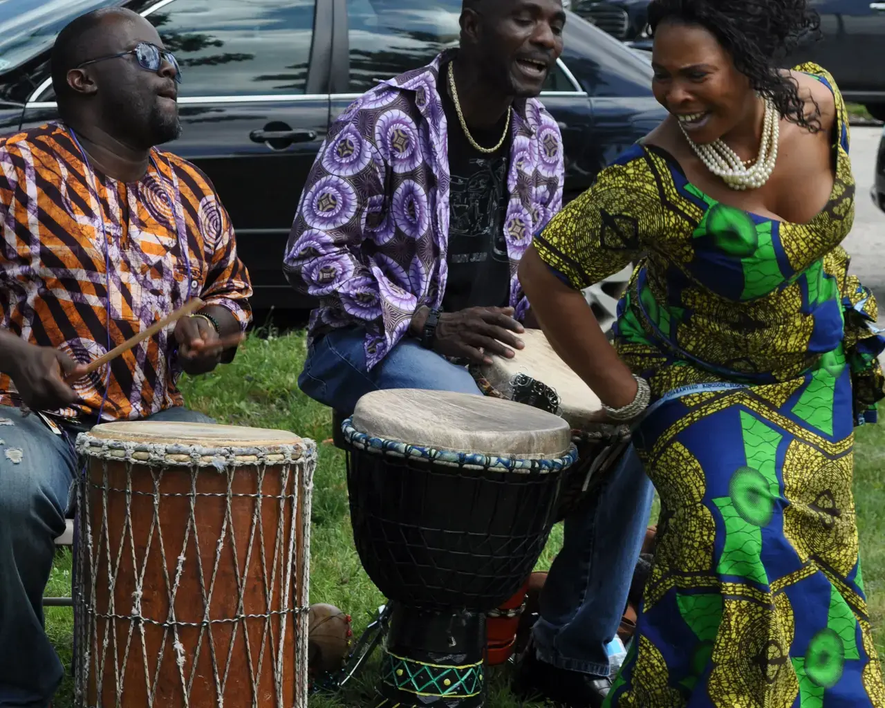 Marie Nyenabo (accompanied by Blamoh Doe and Fernon Flomo) of the Liberian Women&#39;s Chorus for Change at a pop-up concert. Blue Bell Triangle Park, Southwest Philadelphia, June 2014. Photo by Toni Shapiro-Phim.