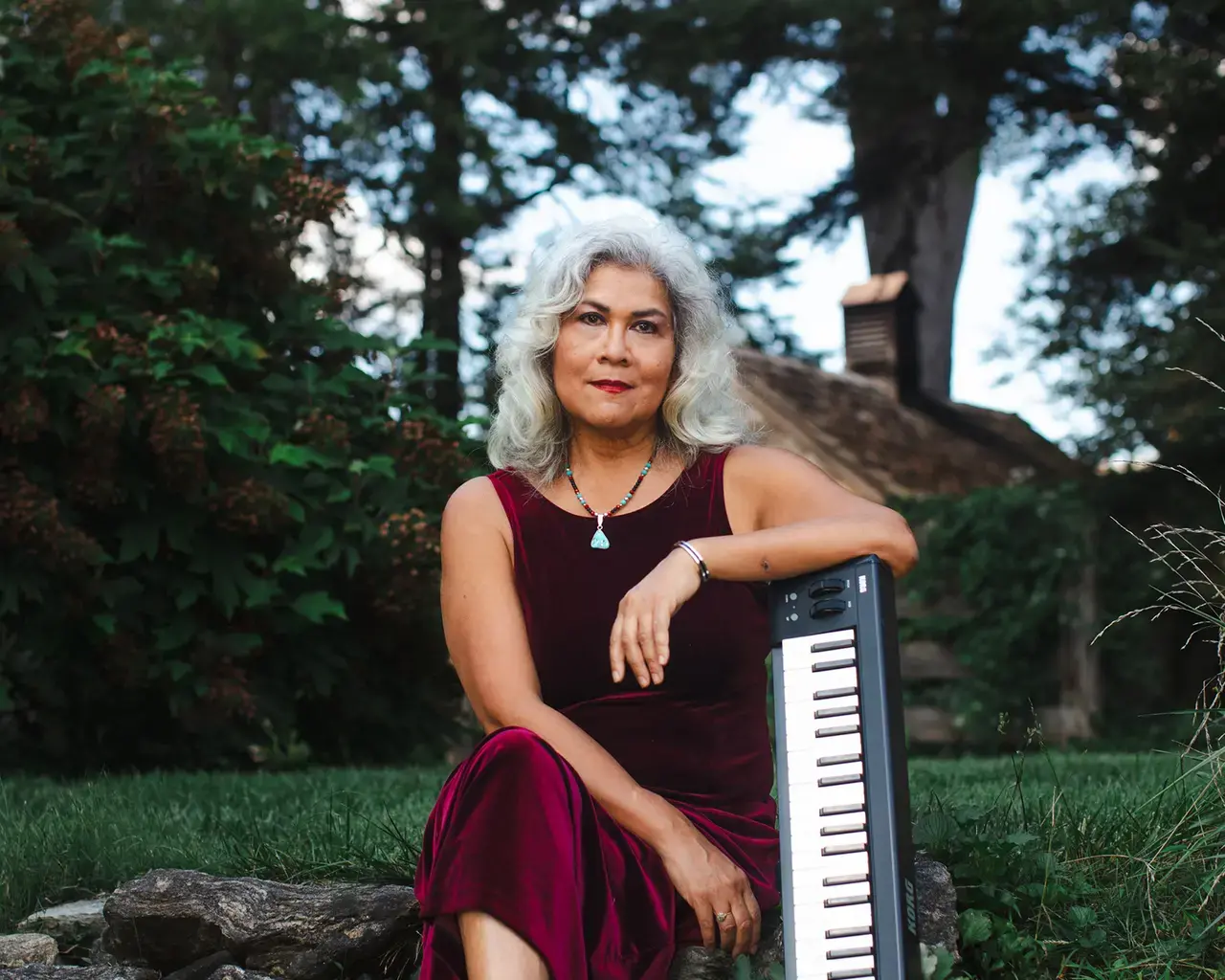 Portrait of Pew Fellow Sumi Tonooka posed outside, leaning on a small keyboard.