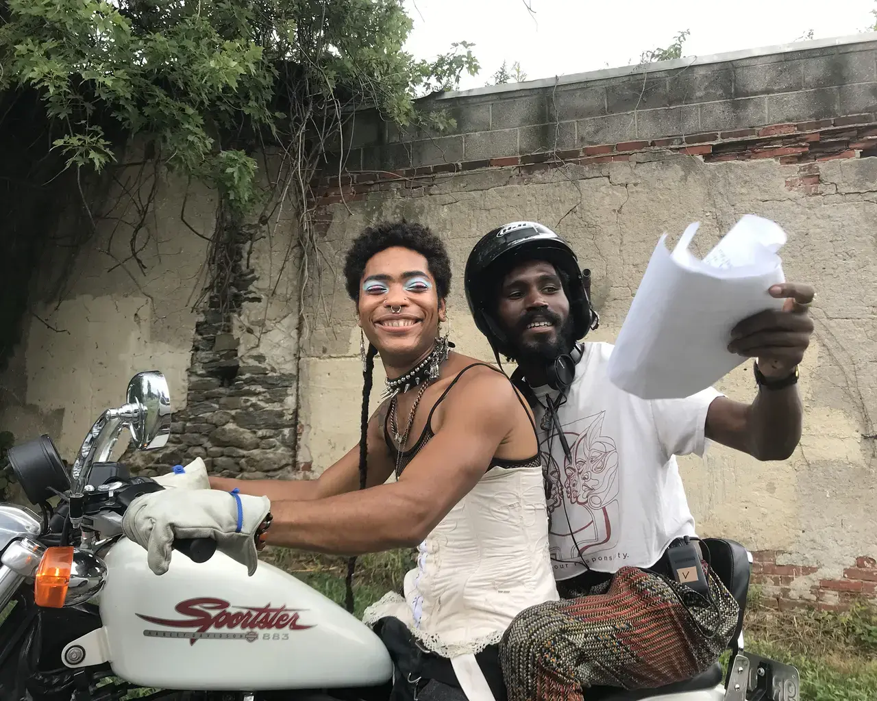 Pew Fellow Vernon Jordan lll rides on the back of a motercycle while holding pages of a script on set of "One Magenta Afternoon."