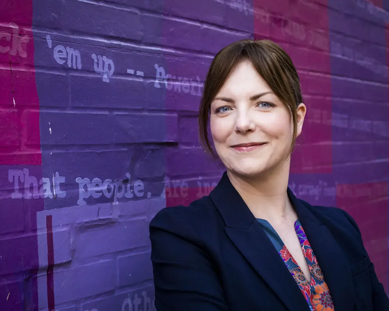 Headshot of director Kathryn MacMillan in front of a richly colored mural.