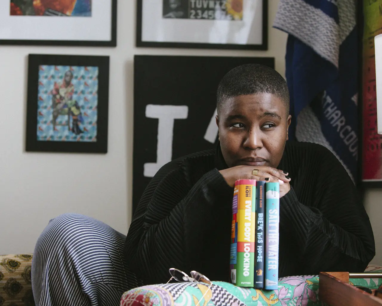 Pew Fellow candice iloh poses with their chin resting on their hands resting on their three published novels.