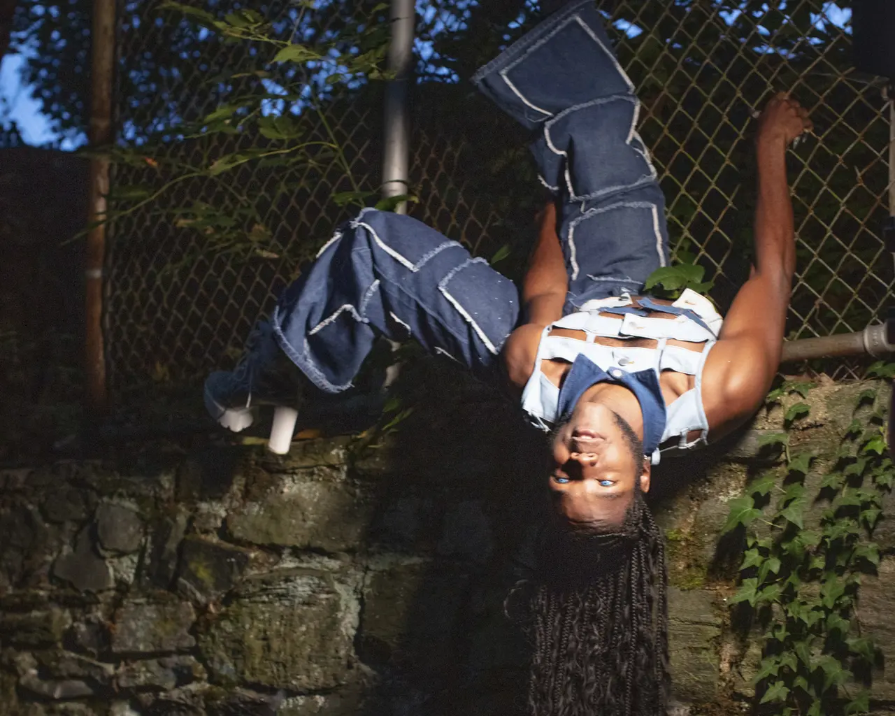 Vitche-Boul Ra hangs upside down from a chain link fence.