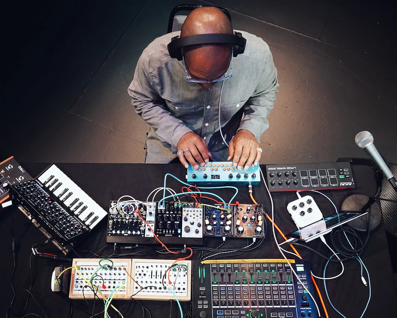 King Britt, seen from above, sits at a table filled with synthesizers, samplers, and a microphone.