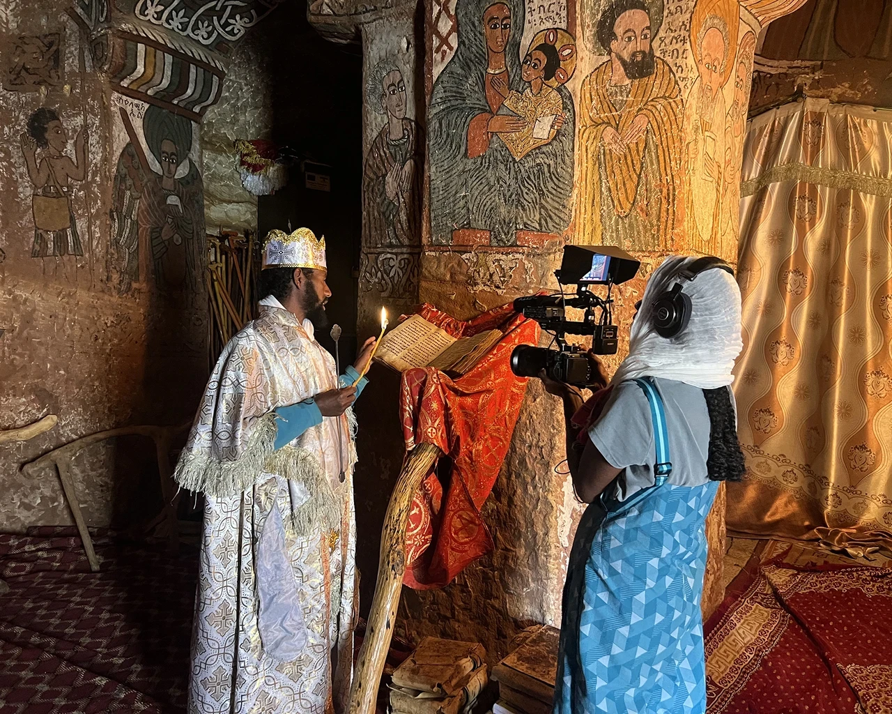 Pew Fellow Sosena Solomon interviews a priest at Abuna Yemata Guh, an ancient monolithic church carved into the sandstone cliffs of Ethiopia’s Tigray region, 2023. Photo by Stephen Battle.