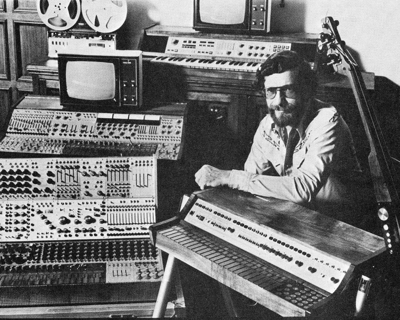 A Photograph of Don Buchla with an assortment of his creations from across his career. Photo courtesy of BuchlaUSA.
