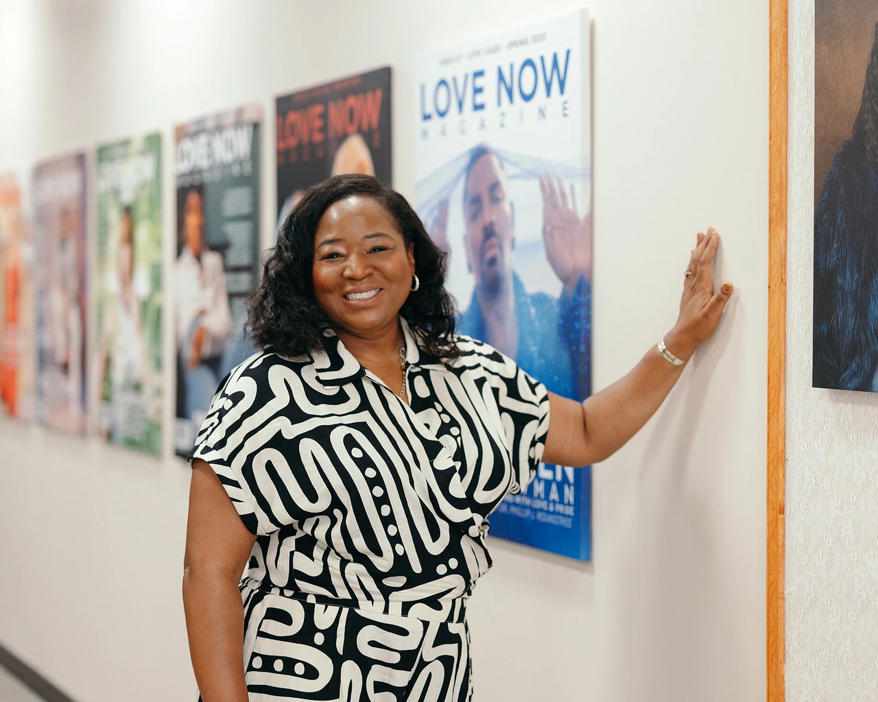 A Black woman in a black and white patterened shirt stands in front of film posters.