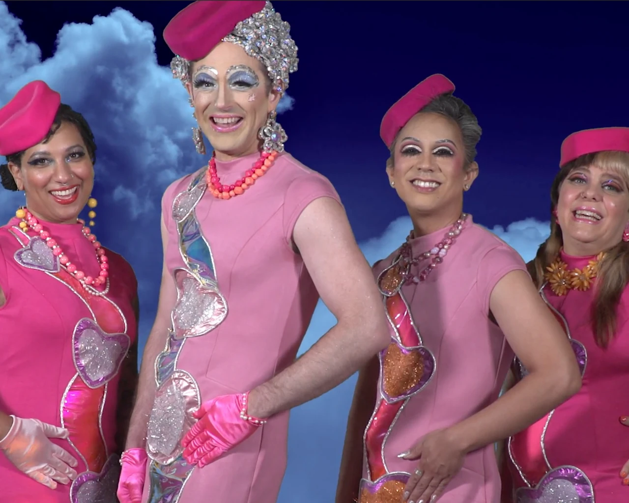 Three women in pink flight attendants outfits and caps stand against a blue sky with clouds.