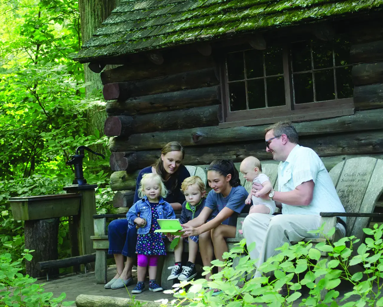 A family learns about the Log Cabin, built in 1908. The Log Cabin was used by Lydia Morris to entertain her friends and contemplate nature among the woodlands. Photo courtesy of Morris Arboretum.