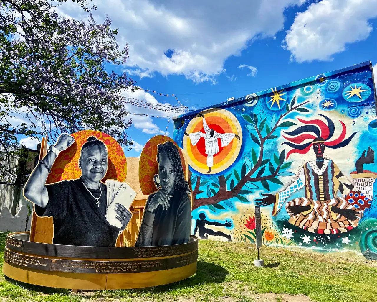 Sculpture: Courtney Bowles and Mark Strandquist, On the Day They Come Home, 2021, part of Staying Power exhibition, The Village of Arts and Humanities, Fairhill-Hartranft neighborhood, Philadelphia, Pennsylvania. Mural: Lily Yeh, Obatala, 2018. Photo courtesy of The Pew Center for Arts &amp; Heritage.
