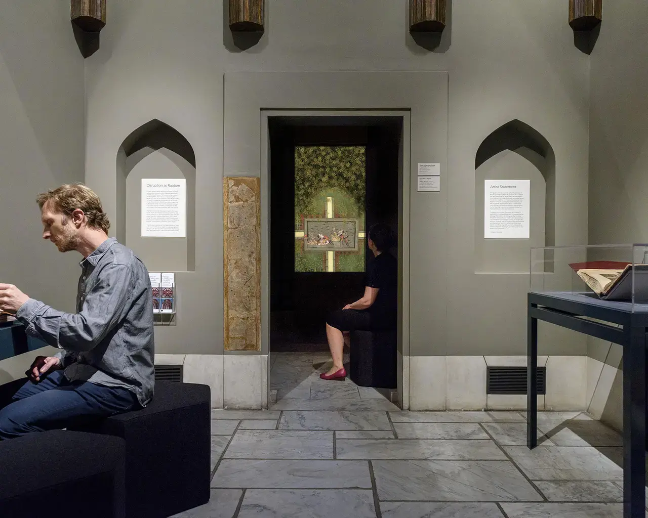 Visitors watch Shahzia Sikander’s contemporary animation of The Rose Garden of Love (center), inspired by the original 1743 manuscript displayed in vitrine (at right), seen in close detail through a replica of the fragile manuscript (at left).