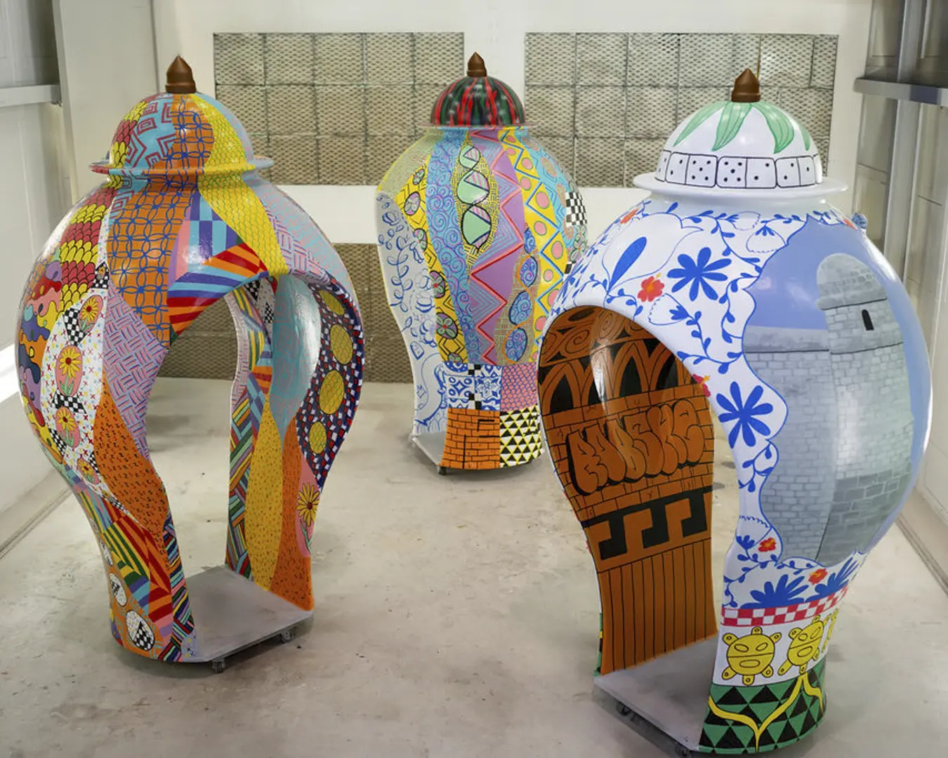 Three large sculptures shaped like clay vessels that have adult-sized walk-ways cut through them. The sculptures are covered in colorful designs reminiscent of graffiti.