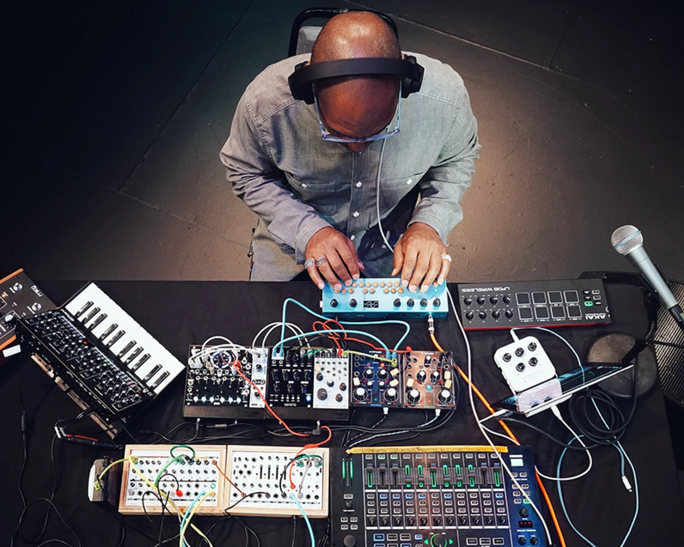 King Britt, seen from above, sits at a table filled with synthesizers, samplers, and a microphone.