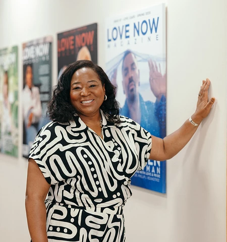 A Black woman in a black and white patterened shirt stands in front of film posters.