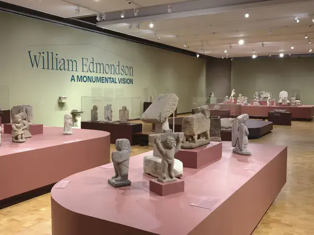 An exhibition of carved stone sculptures on salmon pink pedestals. Painted on the wall in dark green is the exhibition title: "William Edmondson: A Monumental Vision."