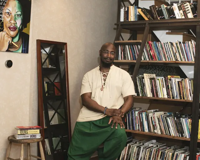 Pew Fellow Phillip B. Williams leaning up against stacks of books.