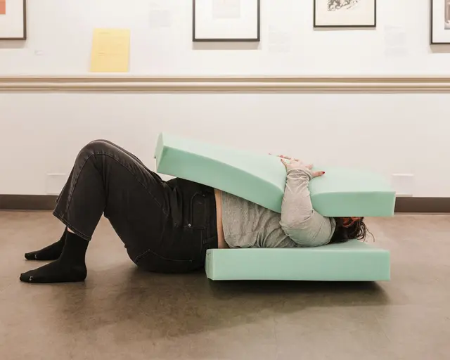 A person lies down on a piece of seagreen foam with another pressed into their face, part of "Blood Baby: Touch Library."